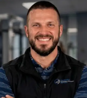 Smiling man with a beard wearing a black vest over a blue striped shirt